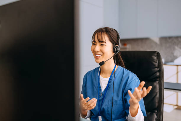 A female healthcare worker wears a headset with a microphone while sitting at her desk in a modern clinic